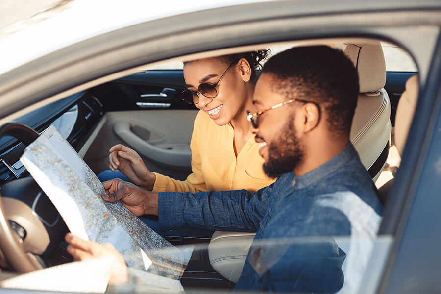 A happy couple looking at a road map sitting in a car traveling on vacation.